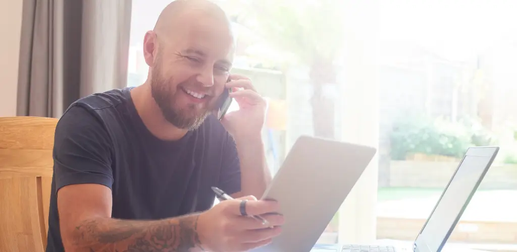 Mies vertailee sähkösopimuksia ja puhelinliittymiä. Mies katsoo tabletilta vertailua ja hymyilee. Toisessa kädessä hän puhuu puhelimessa.